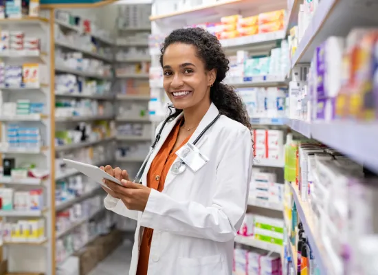 Happy friendly multiethnic pharmacist doing inventory in a provided and modern pharmacy while looking at camera